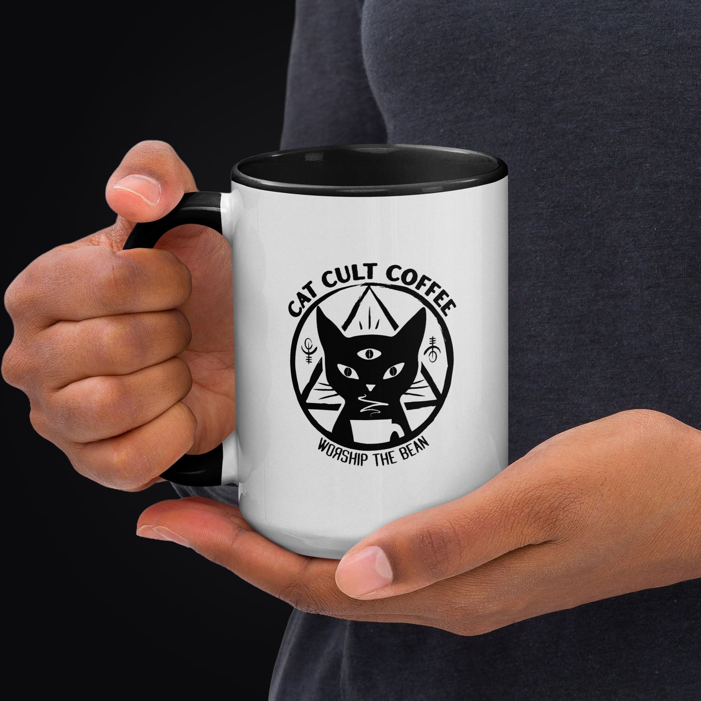 Person holding Cat Cult Coffee Classic Mark 15 oz ceramic coffee mug with a white exterior, black interior, and black handle.